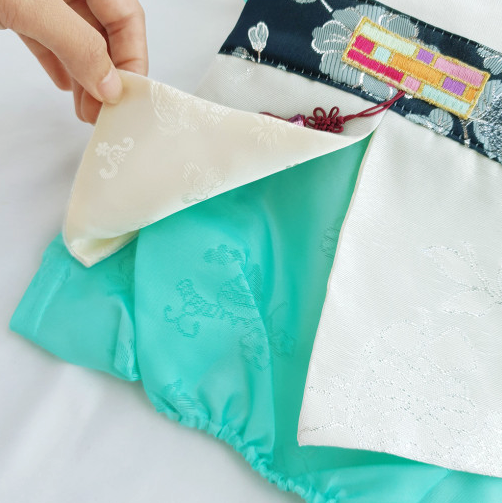 Silver embroidery detail on a white and teal pet hanbok.