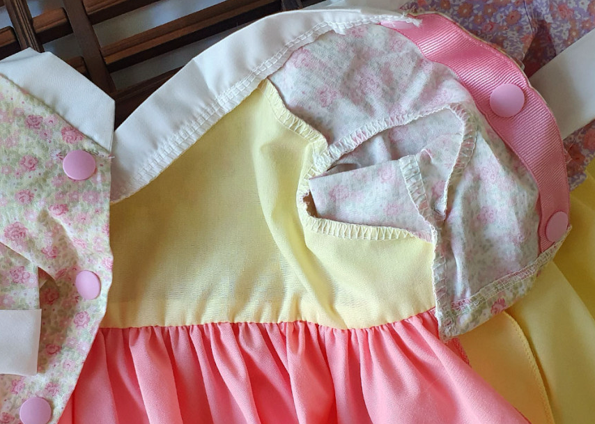 Close-up of the yellow and pink floral bow pet hanbok by NKpup, showing button details and fabric layers.