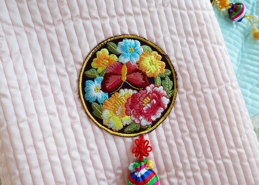 Embroidered floral patch and colorful norigae on a pastel pink quilted pet hanbok vest.