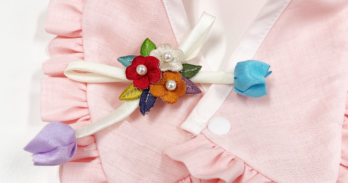 Close-up of a pink NKpup ruffle pet hanbok cape featuring colorful floral embroidery and ribbon details.