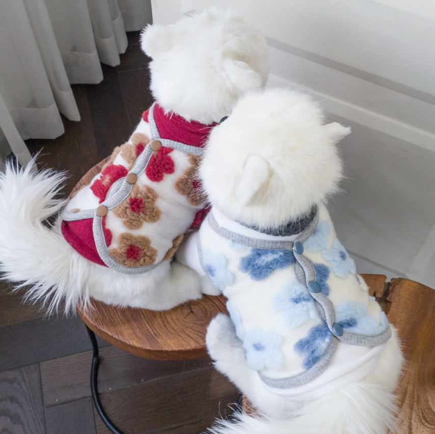 Two white dogs wearing NKpup floral fleece dog vests in red and blue patterns.