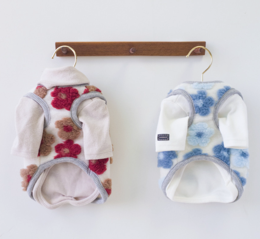 Two NKpup floral fleece dog vests hanging on hangers, one in pink with red flowers and one in white with blue flowers.