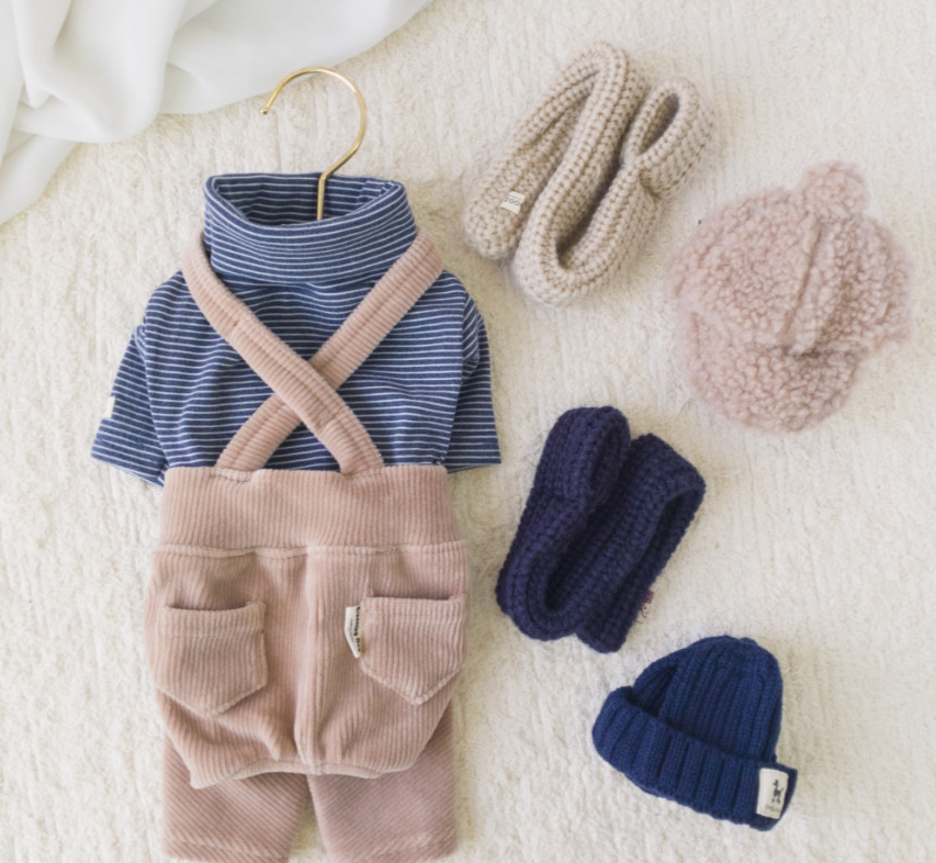 Pink corduroy dog suspender overalls with a blue striped turtleneck shirt and matching knit accessories.