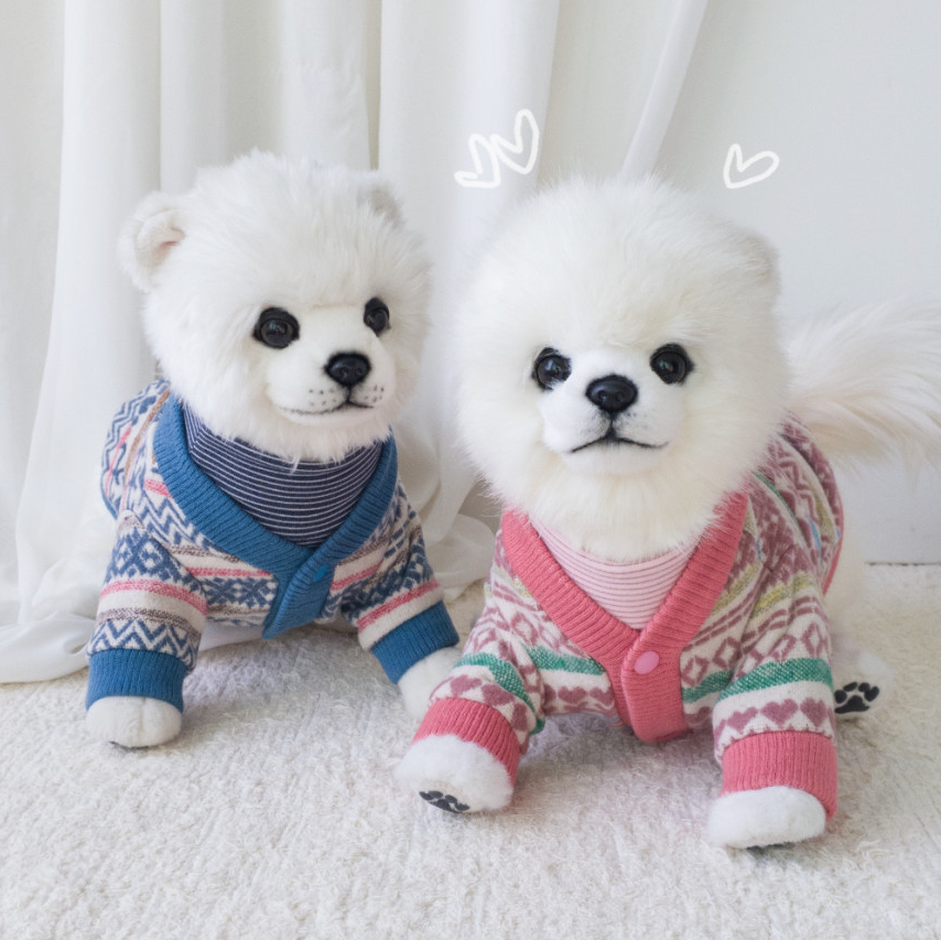 Two white dogs wearing NKpup jacquard knit dog cardigans in blue and pink patterns.