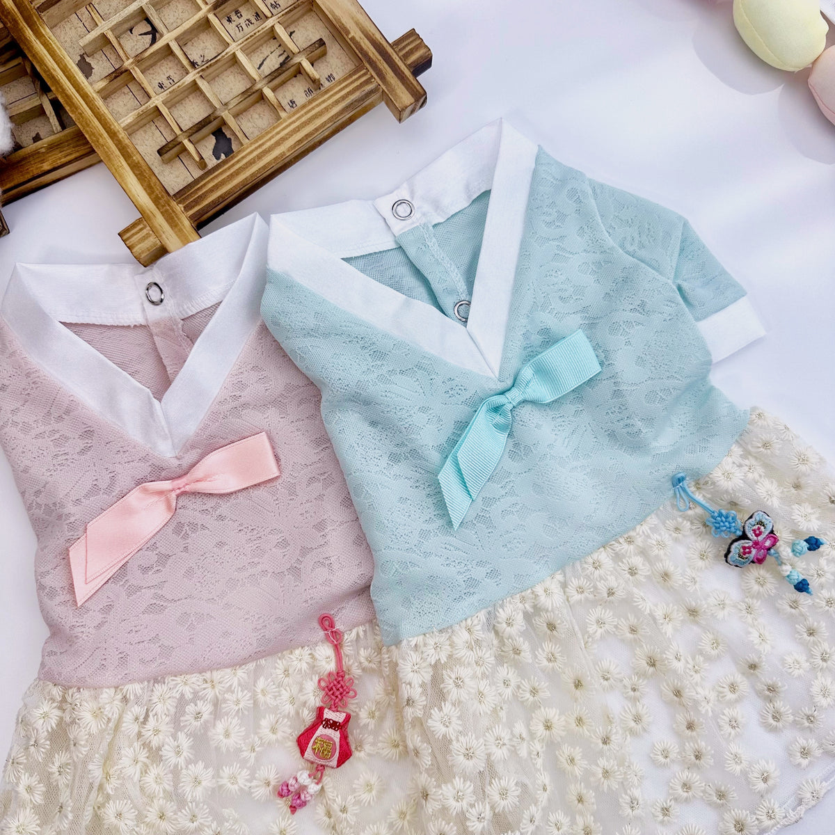 Two lace floral pet hanboks in pink and light blue with decorative norigae tassels.
