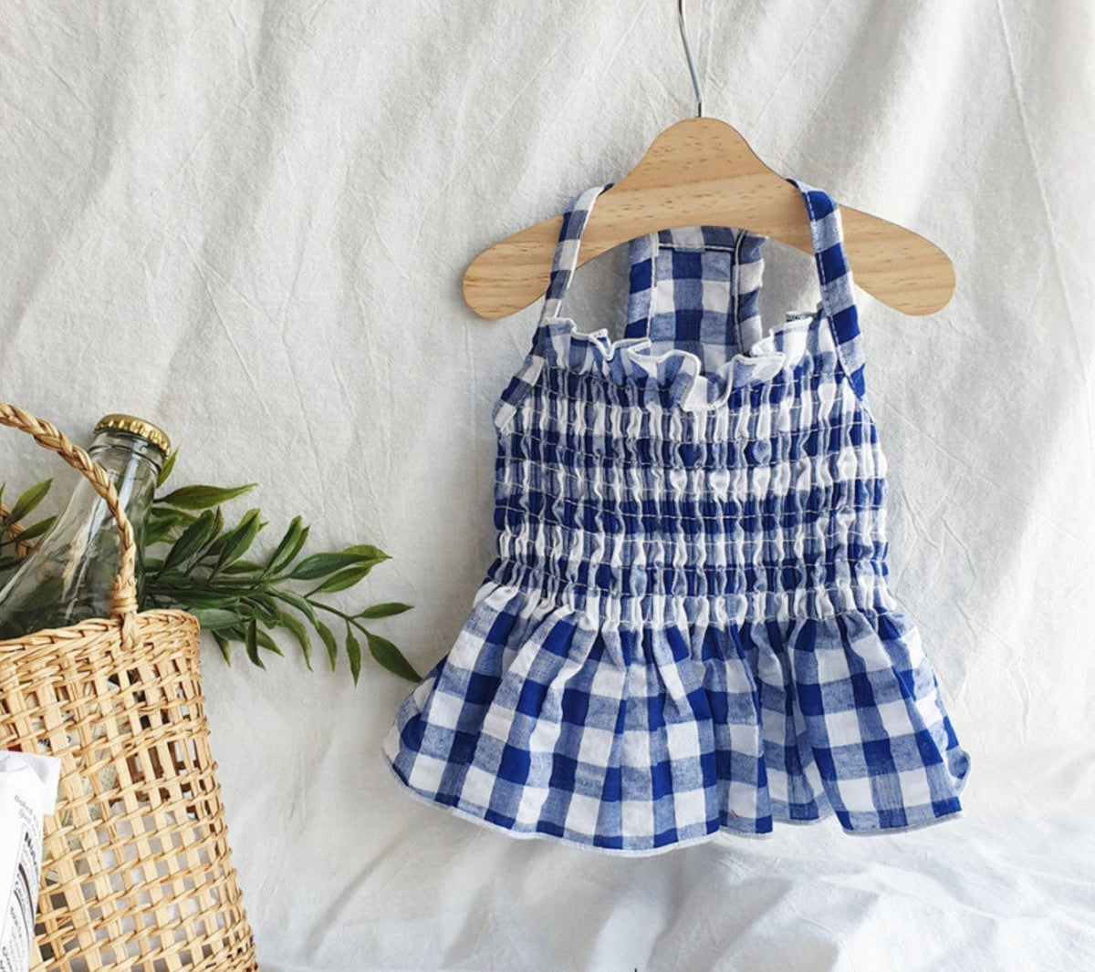Blue and white gingham smocked dog dress hanging on a wooden hanger