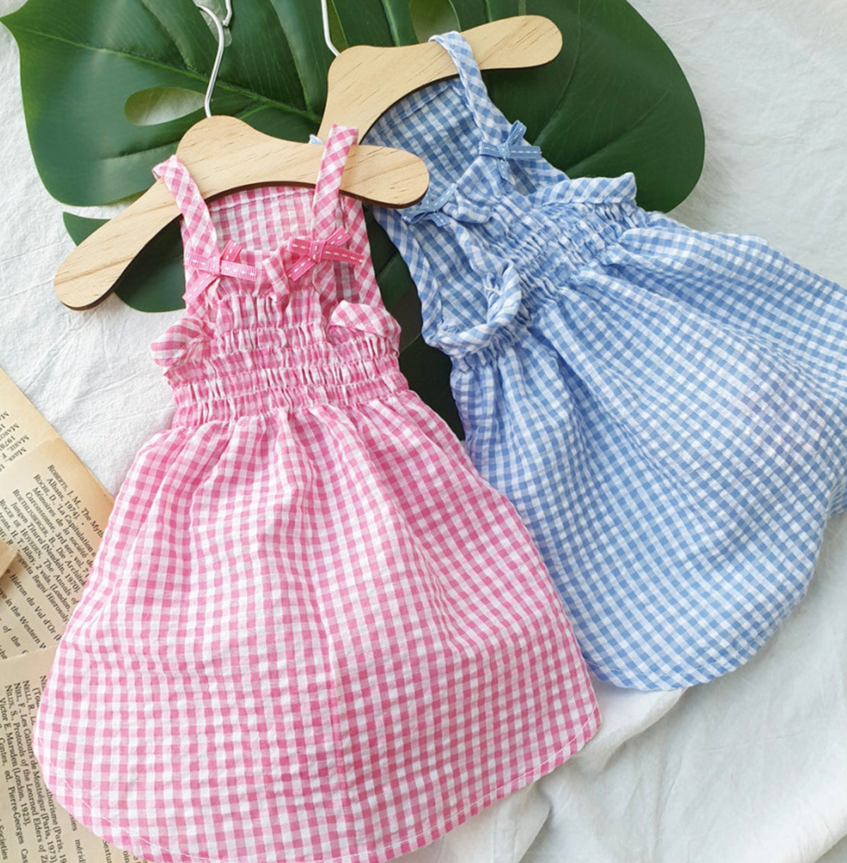 Two vintage gingham dog dresses in pink and blue with smocked detailing and bow straps.