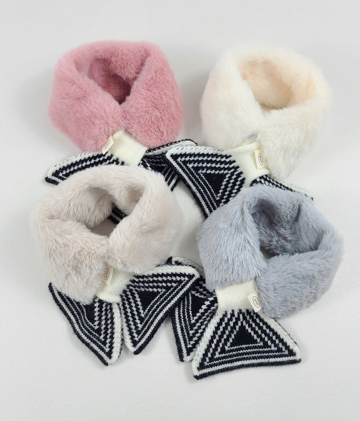 Four NKpup fur mufflers in pink, white, cream, and grey with black and white geometric patterns.