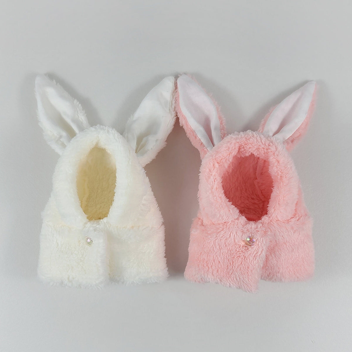 Two plush rabbit hoodie warmer hats for pets in white and pink colors.