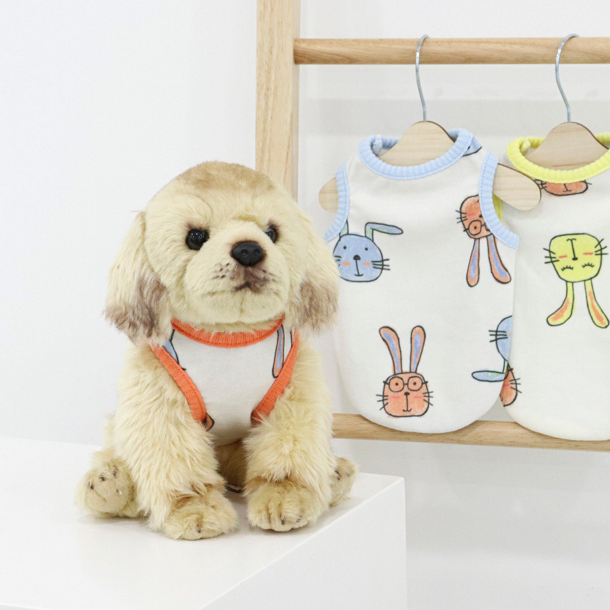White sleeveless dog top with colorful rabbit patterns hanging on a wooden rack.