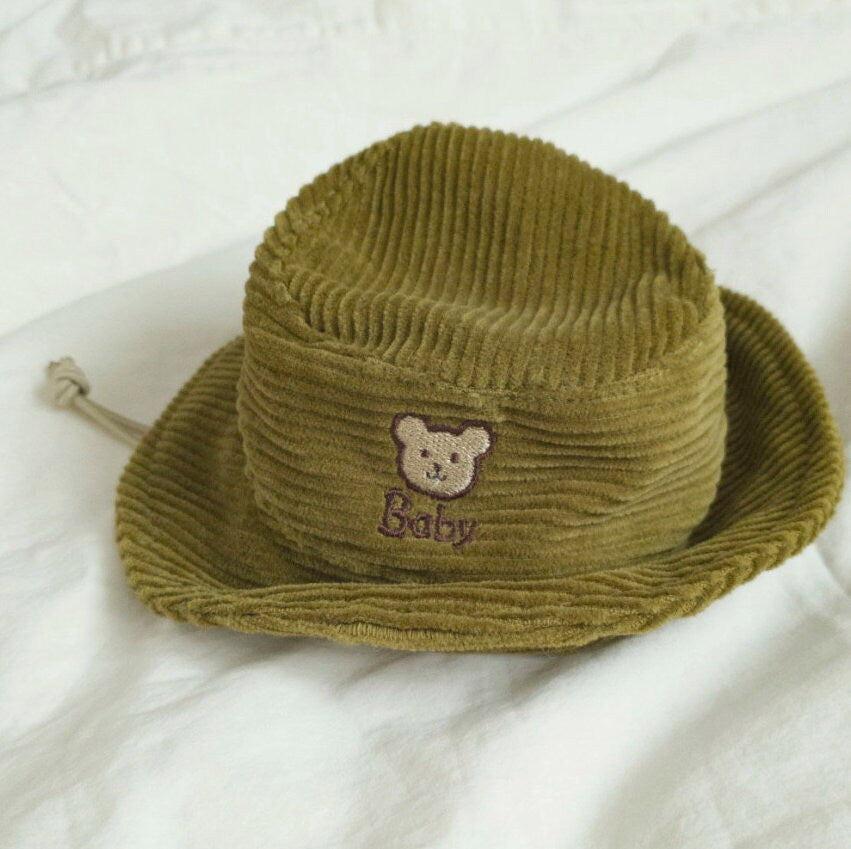 Olive green corduroy bucket hat for dogs featuring a brown bear embroidery and the word Baby