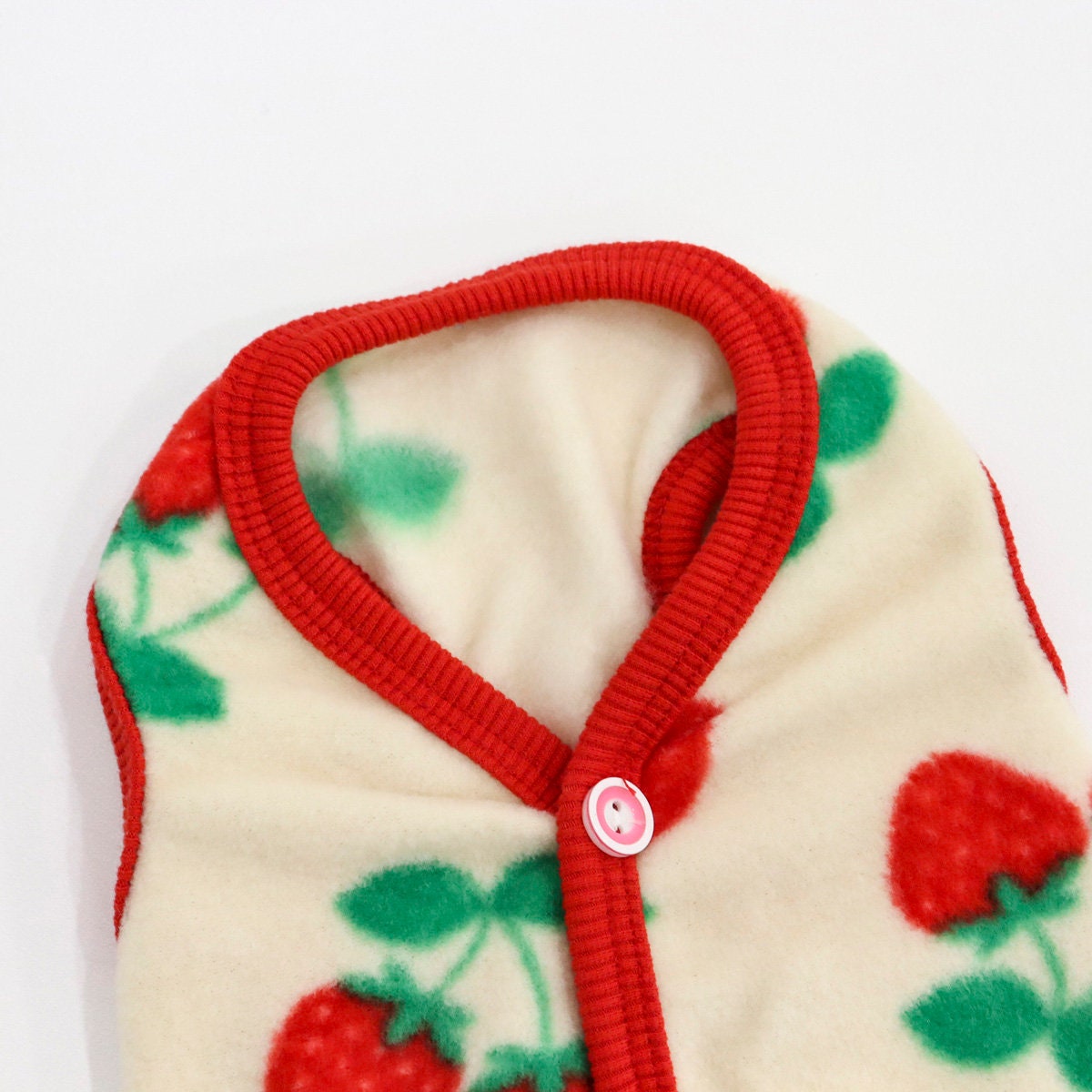 Strawberry pattern boa fleece dog vest with red trim and a single pink button