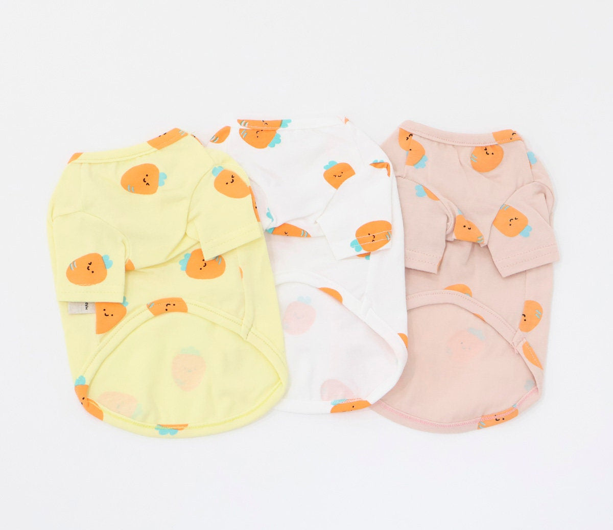 Three NKpup carrot print dog shirts in yellow, white, and pink.