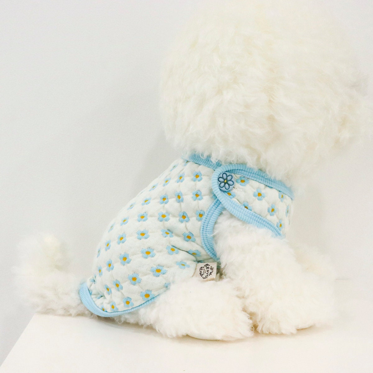 White quilted dog vest with a blue daisy pattern and light blue trim.