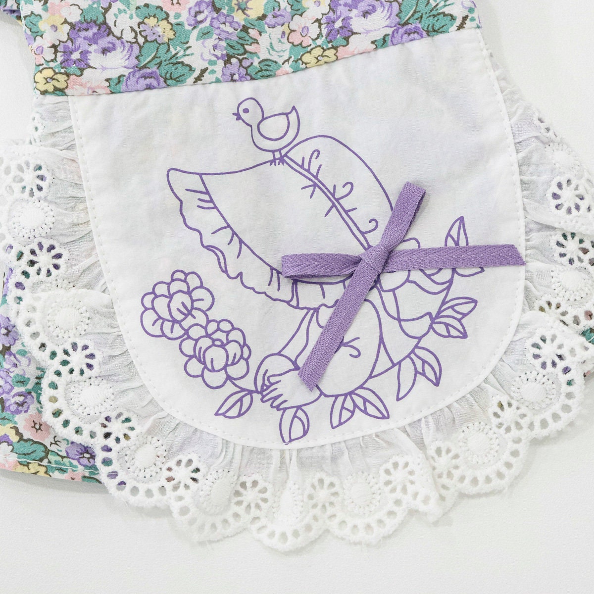 Floral pinafore dog dress with white lace trim and purple bird illustration