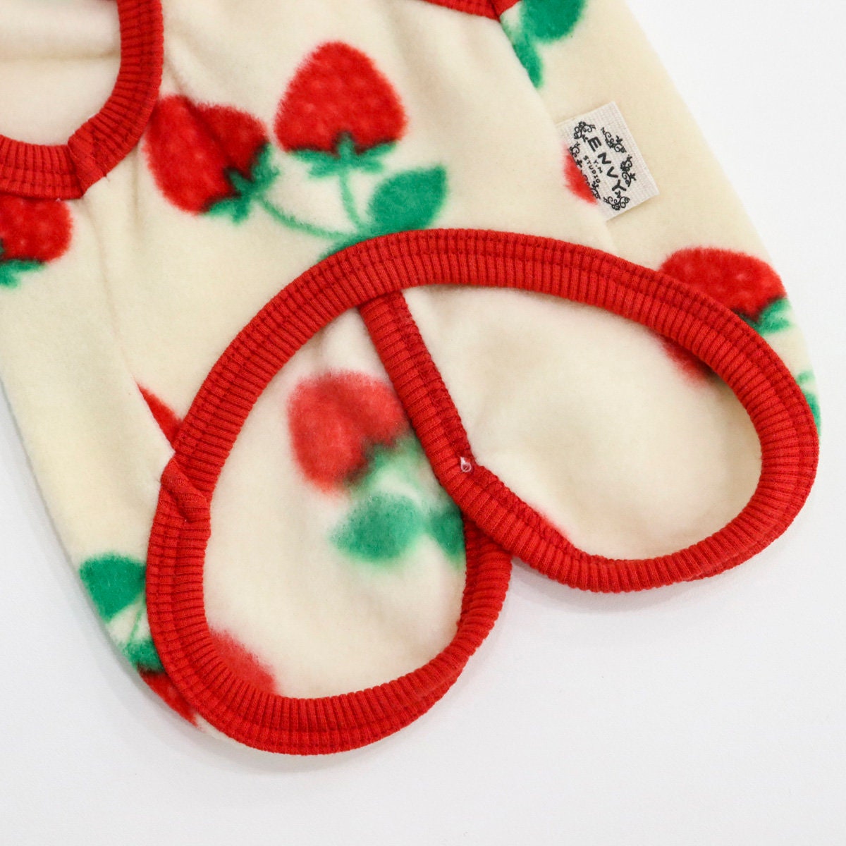 Cream-colored strawberry print fleece dog vest with red ribbed trim.
