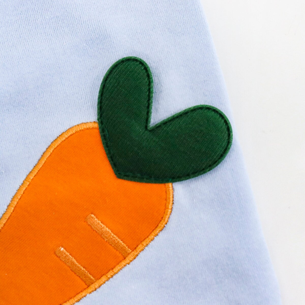 Close-up of a light blue NKpup dog shirt featuring an orange heart-shaped carrot applique.
