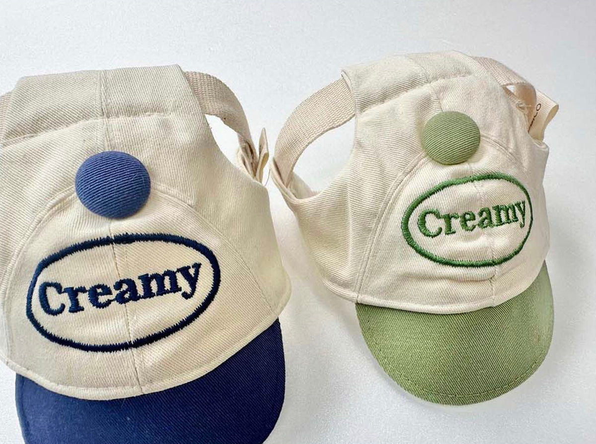 Two NKpup creamy dog cap hats with embroidered Creamy text and contrasting colored brims.