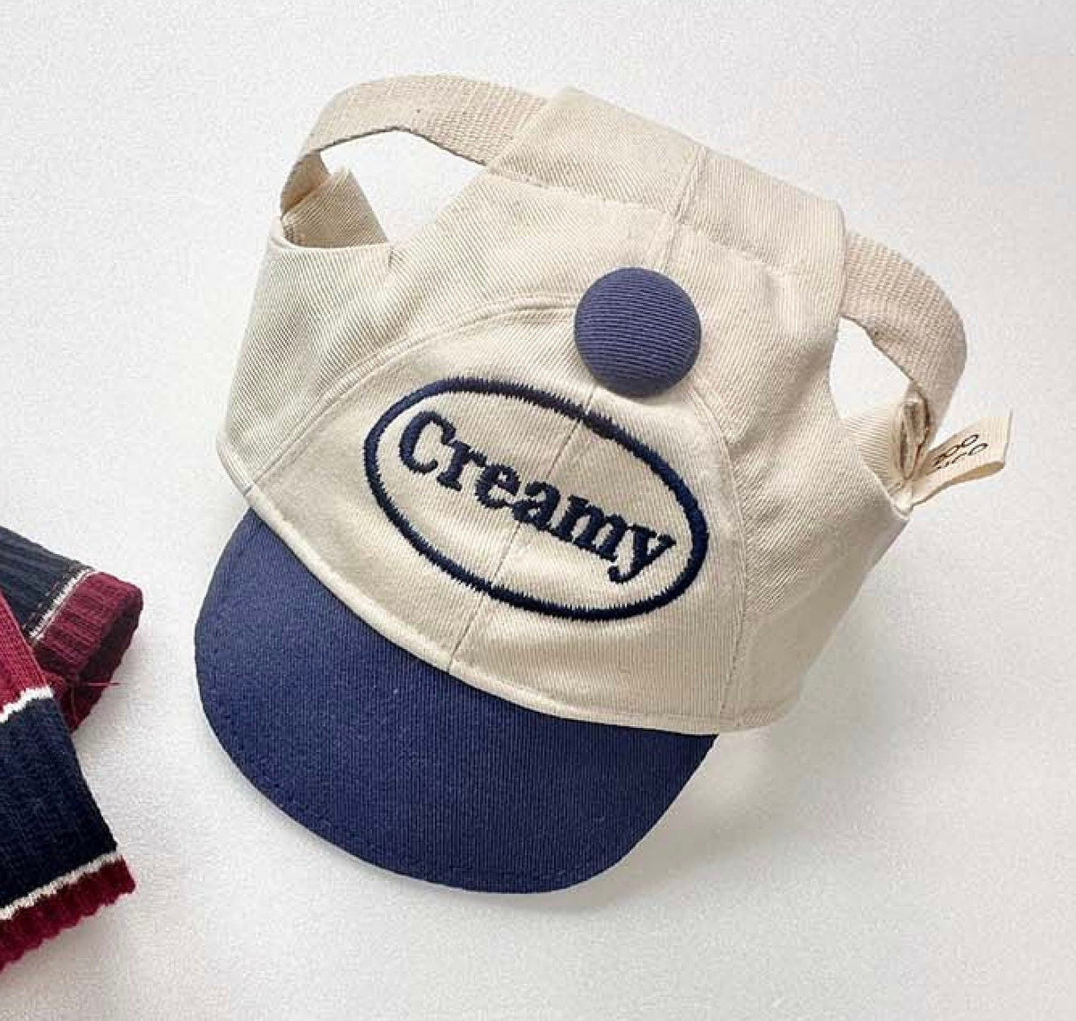 Creamy dog cap hat in cream and navy blue with embroidered text and a decorative button.