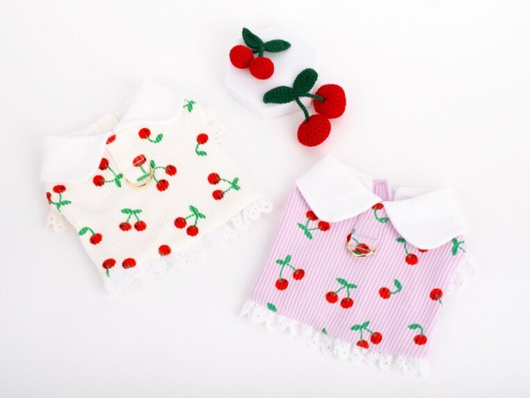 Two cherry patterned pet dresses, one white and one pink, featuring white collars and lace trim.
