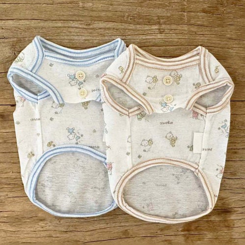 Two NKpup GOTS organic jacquard dog shirts in pastel blue and beige with cute character patterns.