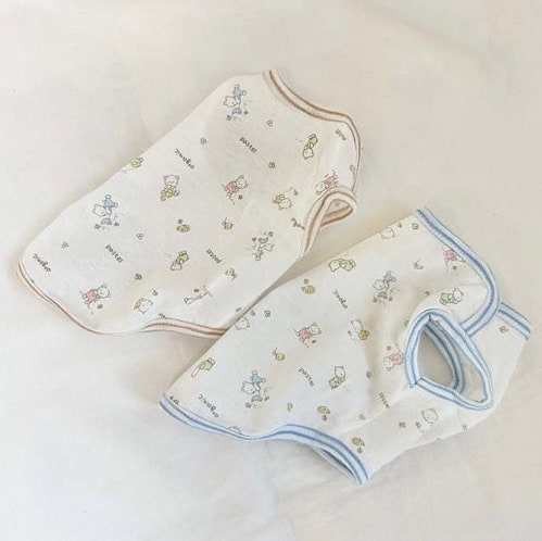 Two NKpup GOTS organic jacquard dog shirts in white with pastel animal patterns and contrasting trim.