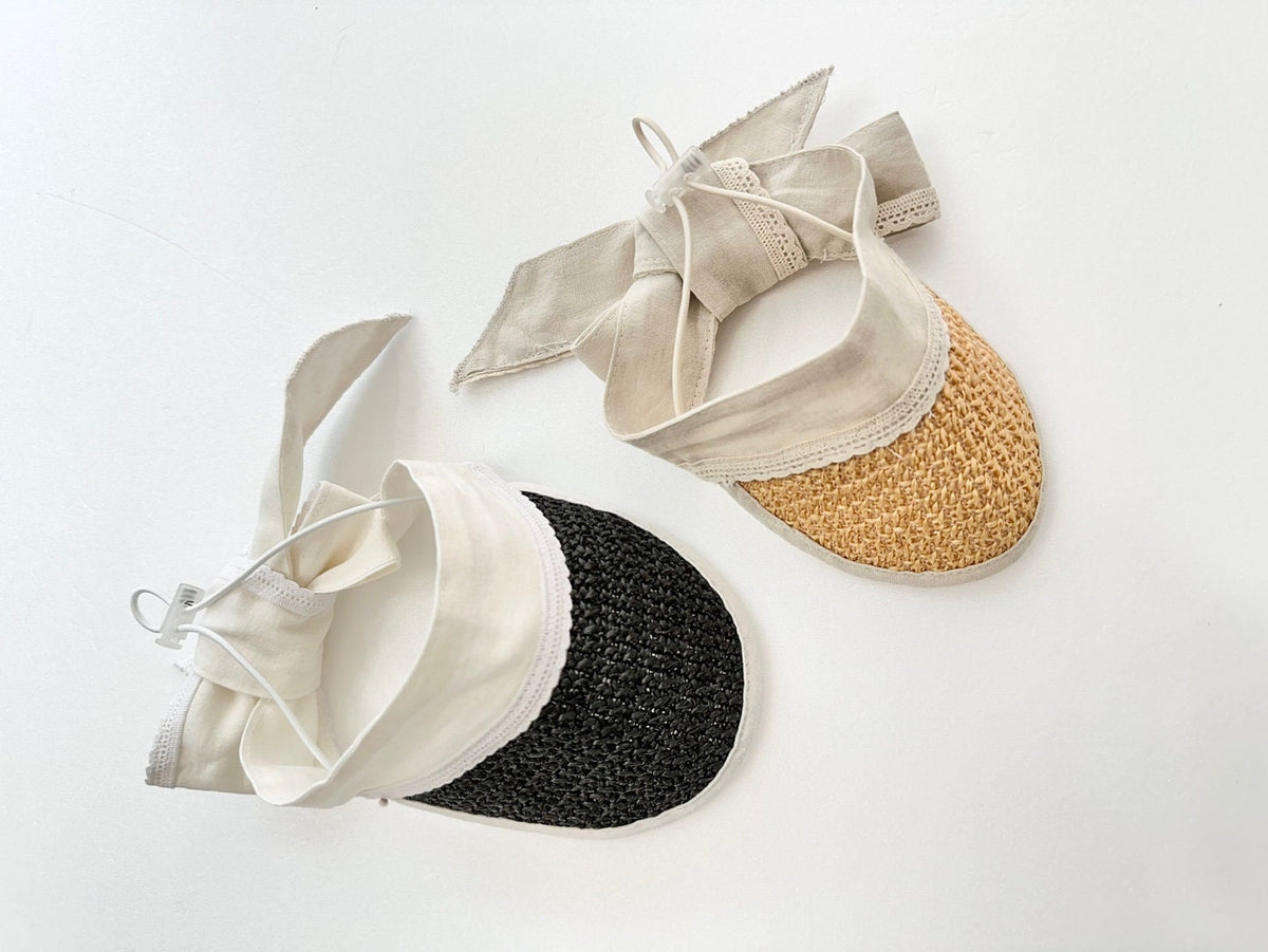 Two charming straw sun hats for pets with cream fabric ties, one in black and one in natural tan.