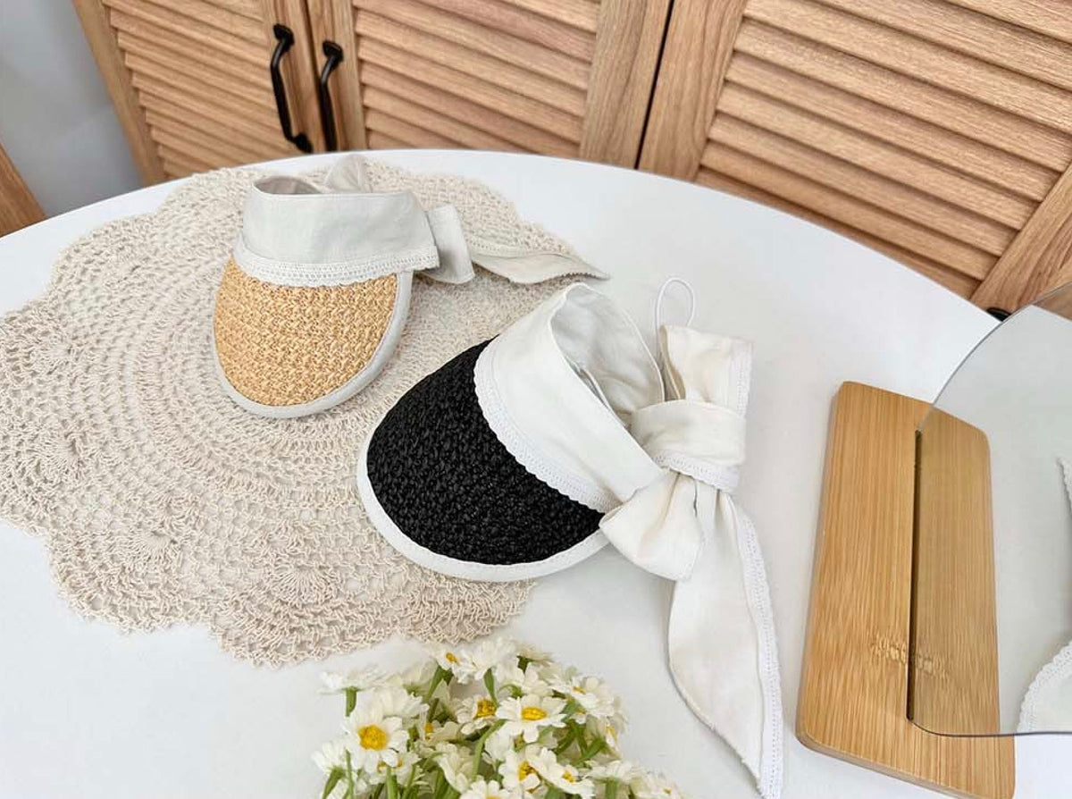 Two straw sun hats for pets, one in natural tan and one in black, featuring white fabric ties.