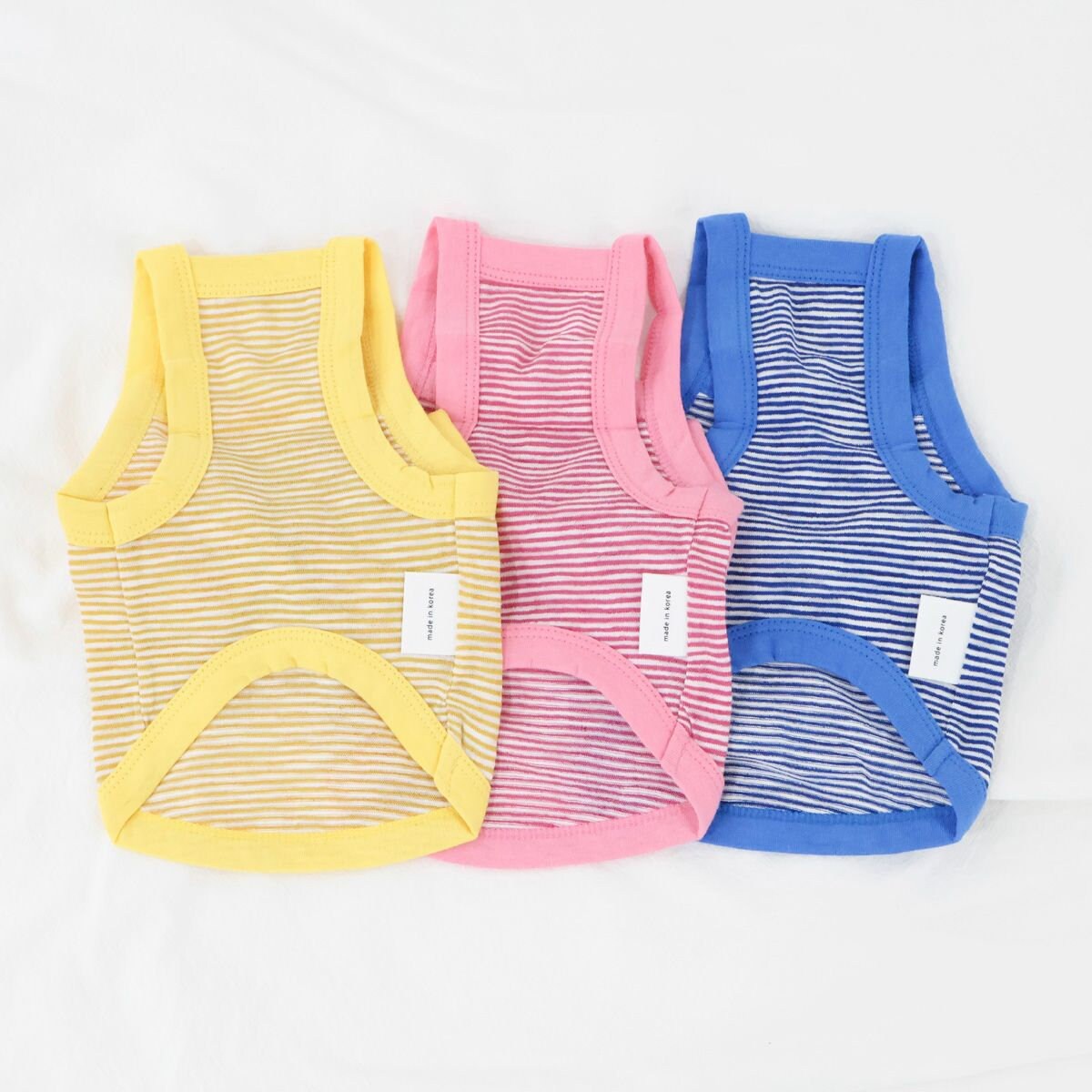 Three NKpup Ribbon Stripe Top dog shirts in yellow, pink, and blue.