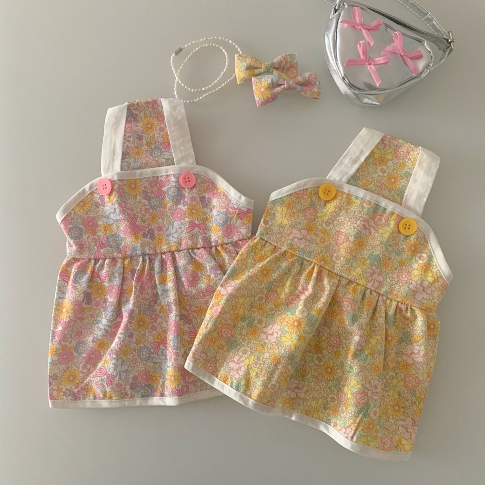 Two NKpup vintage floral pet dresses in pink and yellow patterns with matching accessories.