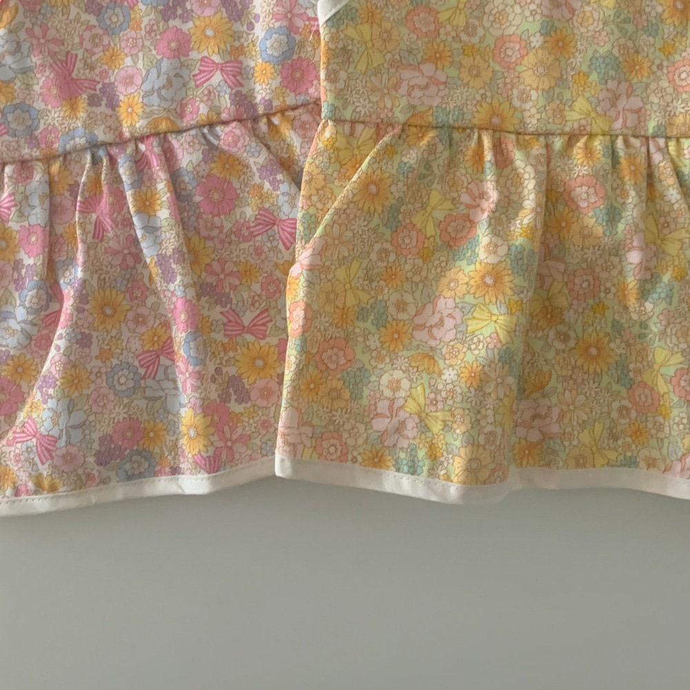 Vintage floral pattern pet dress with pink and yellow flower designs and ruffled hem.