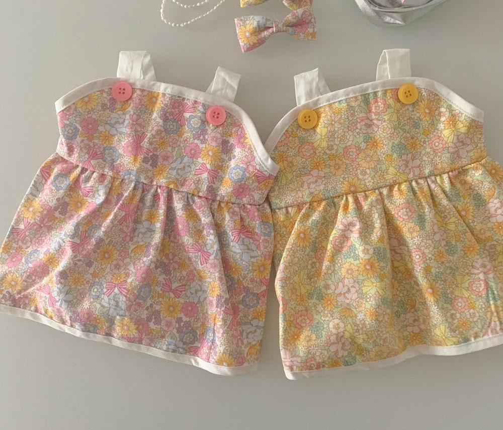 Two vintage floral dog dresses with pink and yellow patterns and button details.