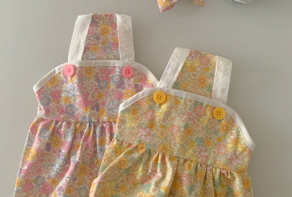 Vintage floral print pet dresses in pink and yellow with white straps and decorative buttons.