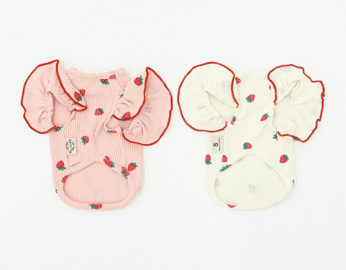 Two strawberry pattern dog shirts with ruffled sleeves, one in pink and one in cream.