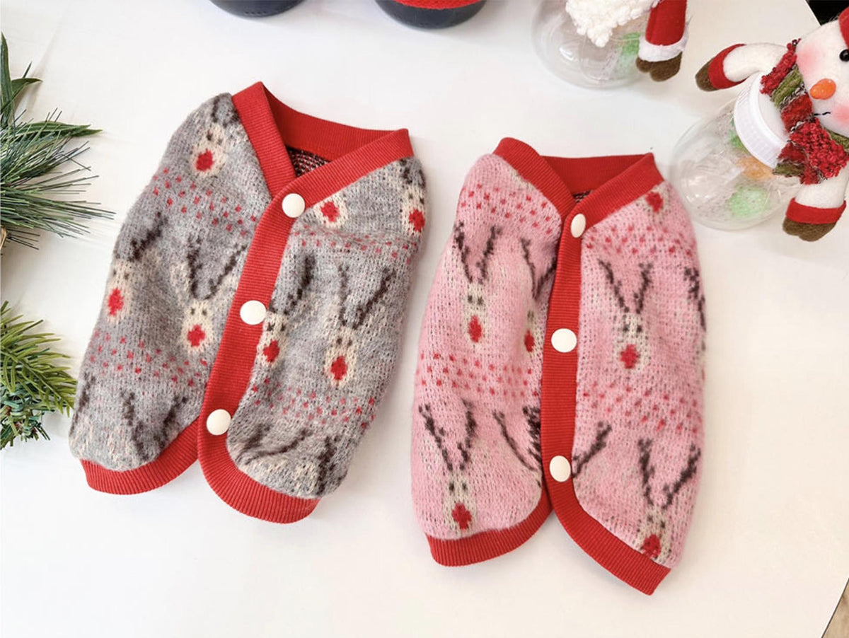 Two Christmas reindeer knit dog vests, one grey and one pink with red trim and white buttons.