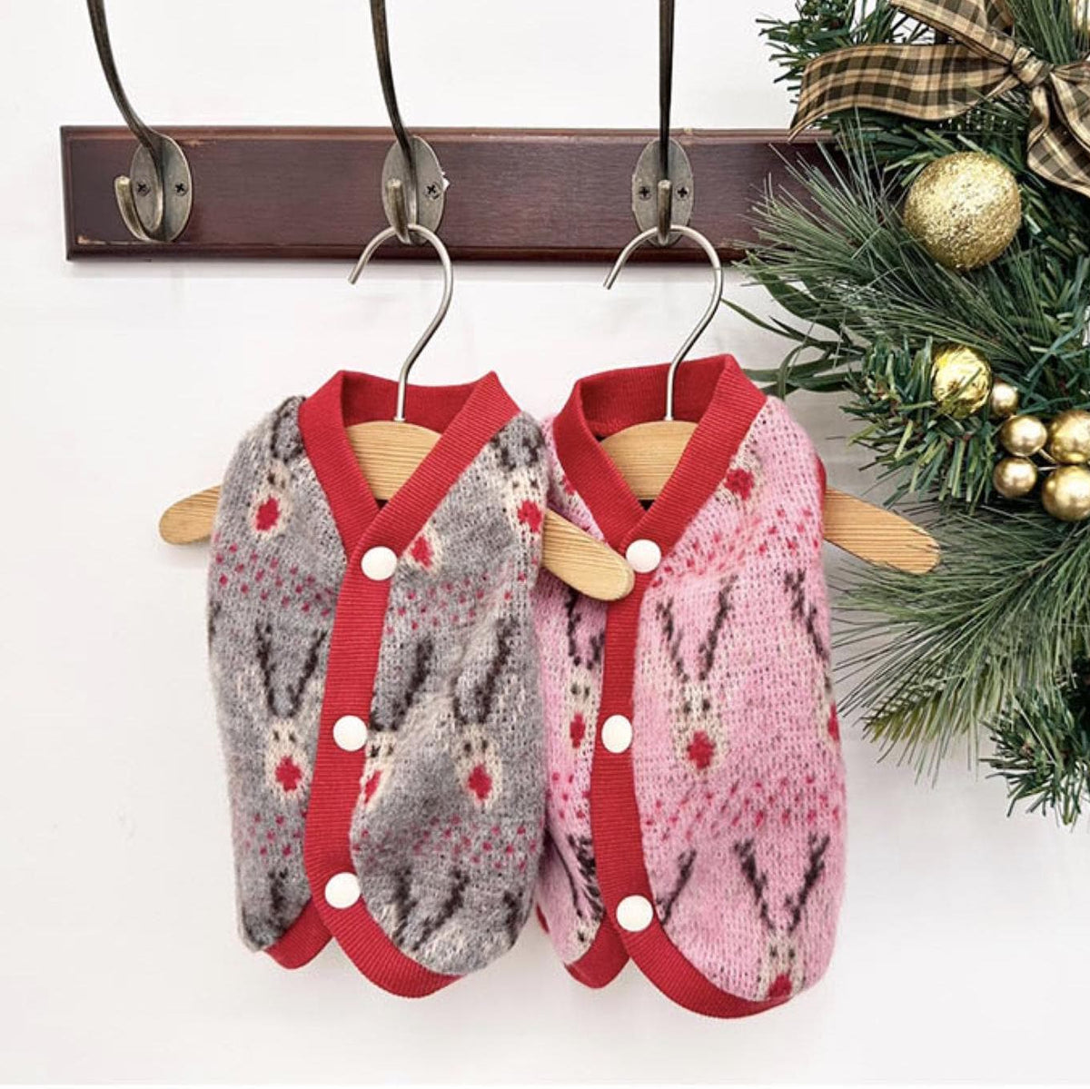 Two Christmas reindeer knit dog vests in grey and pink with red trim and button closures.