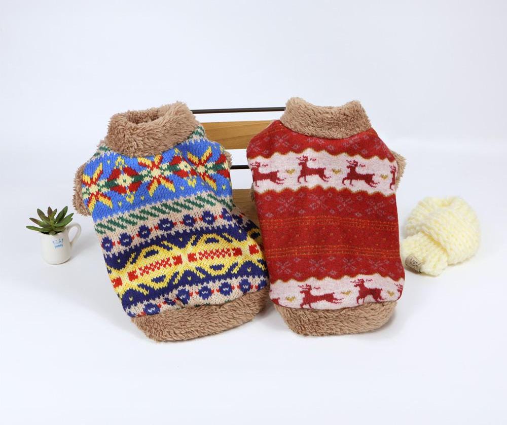 Two Nordic fleece dog sweatshirts, one blue with colorful patterns and one red with reindeer motifs.