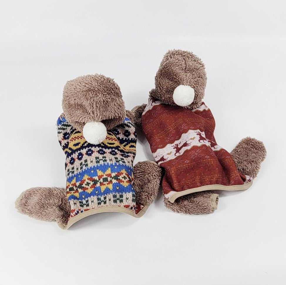 Two NKpup Nordic Bear Dog Overalls in blue and red Fair Isle knit patterns with plush bear hoods.