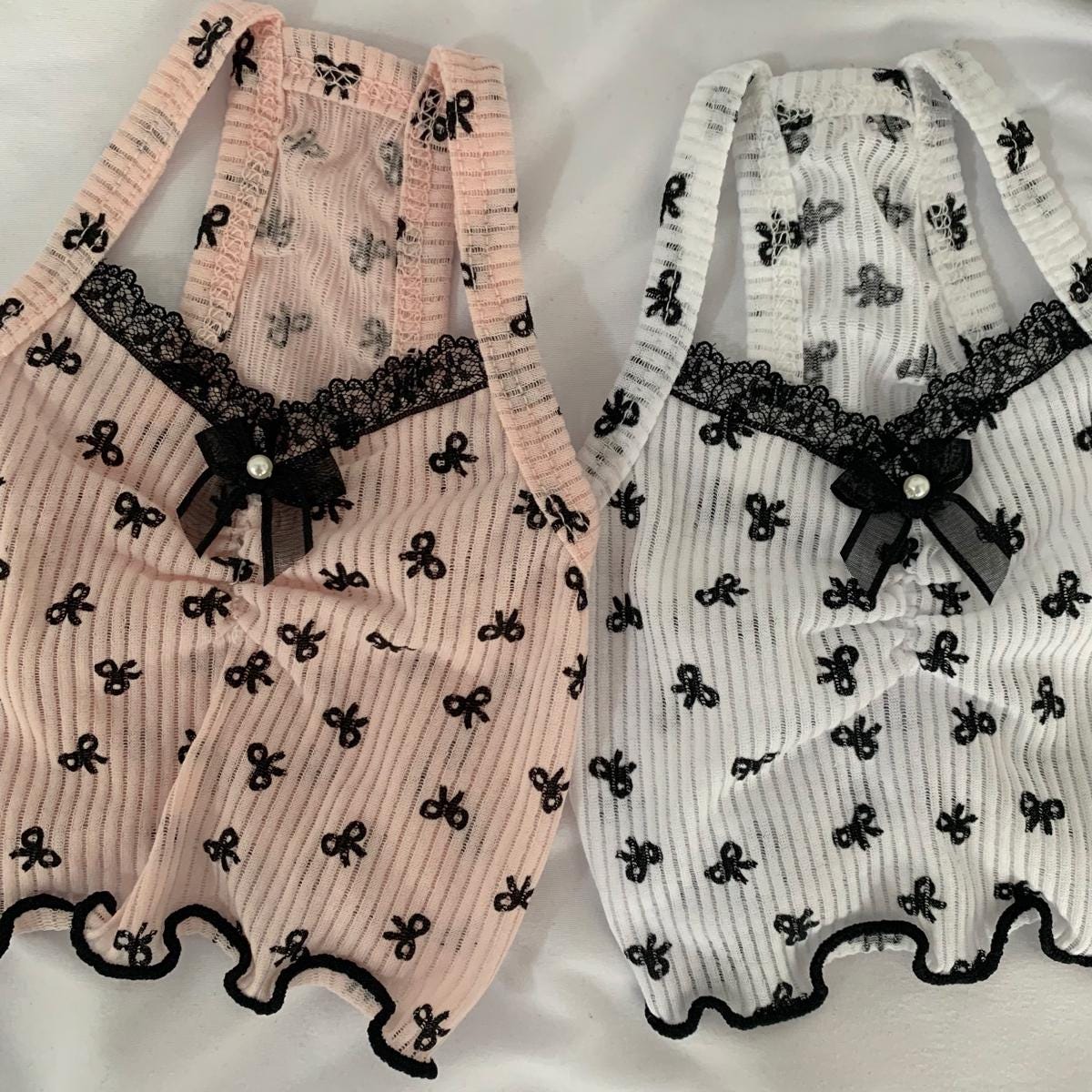 Two NKpup bow crop top pet shirts, one pink and one white, featuring black lace trim and bow details.