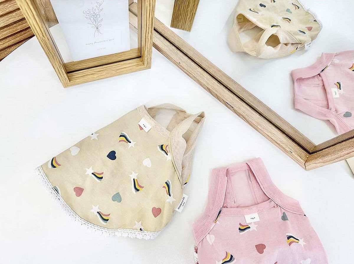 Rainbow print dog dresses in cream and pink colors.
