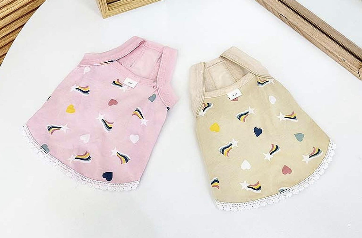 Two NKpup rainbow print dog dresses in pink and beige with lace trim.