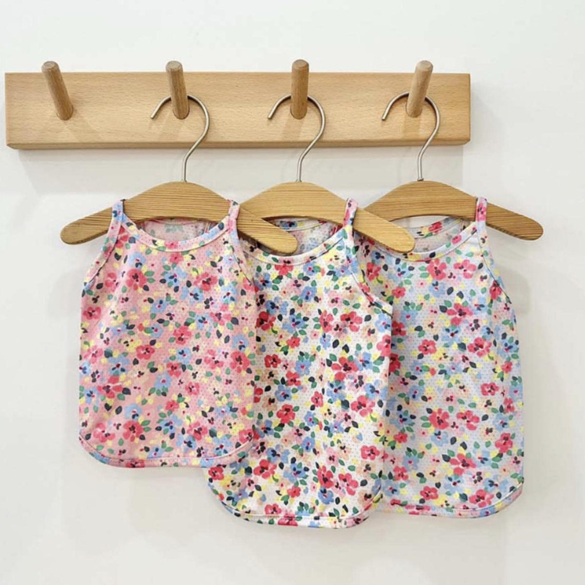 Three NKpup floral cooling mesh dog shirts in colorful flower patterns hanging on wooden hangers.