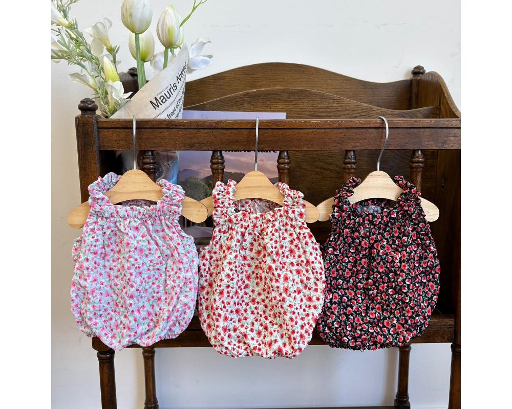 Three NKpup ruffle neck floral dog rompers in pink, red, and black patterns hanging on a wooden shelf.
