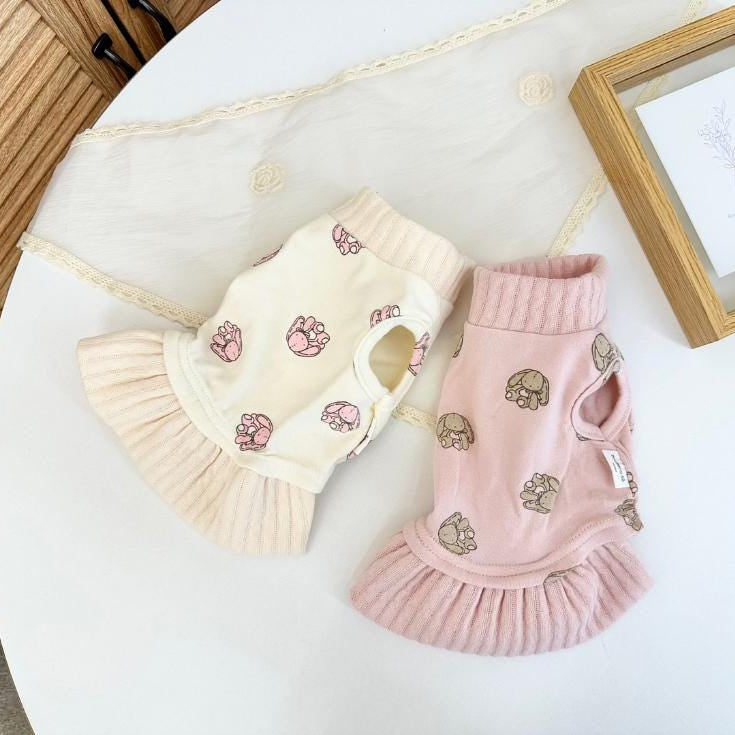 Two NKpup bunny dresses for pets in cream and pink with paw print patterns and ruffled hems.