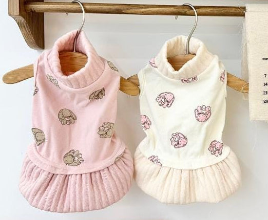 Two NKpup bunny dress pet shirts, one pink and one cream, featuring paw print patterns.