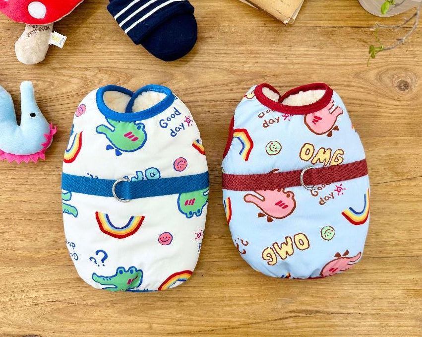 Two NKpup OMG D-Ring padded dog vests, one white with green dinosaur patterns and one blue with pink pig patterns.