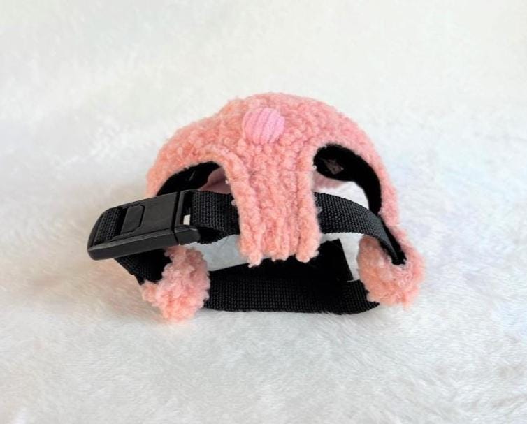 Pink teddy fleece cap for pets with an adjustable black strap and a small decorative button.