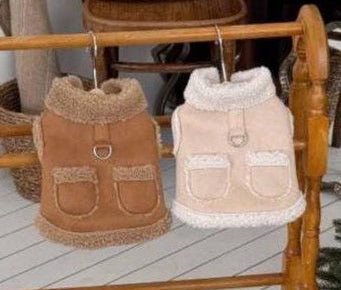 Two cozy pocket shearling vests for pets in tan and cream colors hanging on a wooden rack.