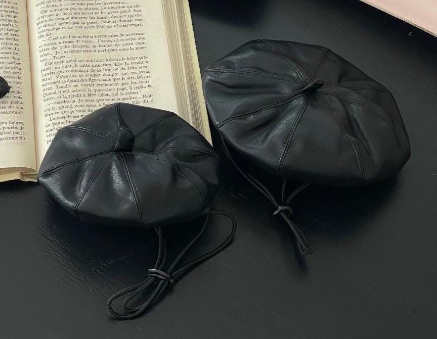 Two black NKpup faux leather dog beret hats with adjustable chin ties.