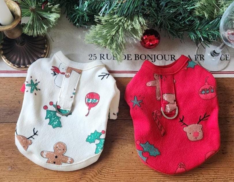 Two Christmas D-Ring dog shirts, one white with gingerbread and snowman patterns and one red with festive motifs.